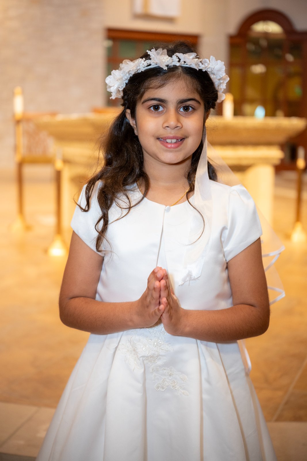 Young girl in her First Communion dress standing in a church with hands in prayer, captured by Zan Visuals