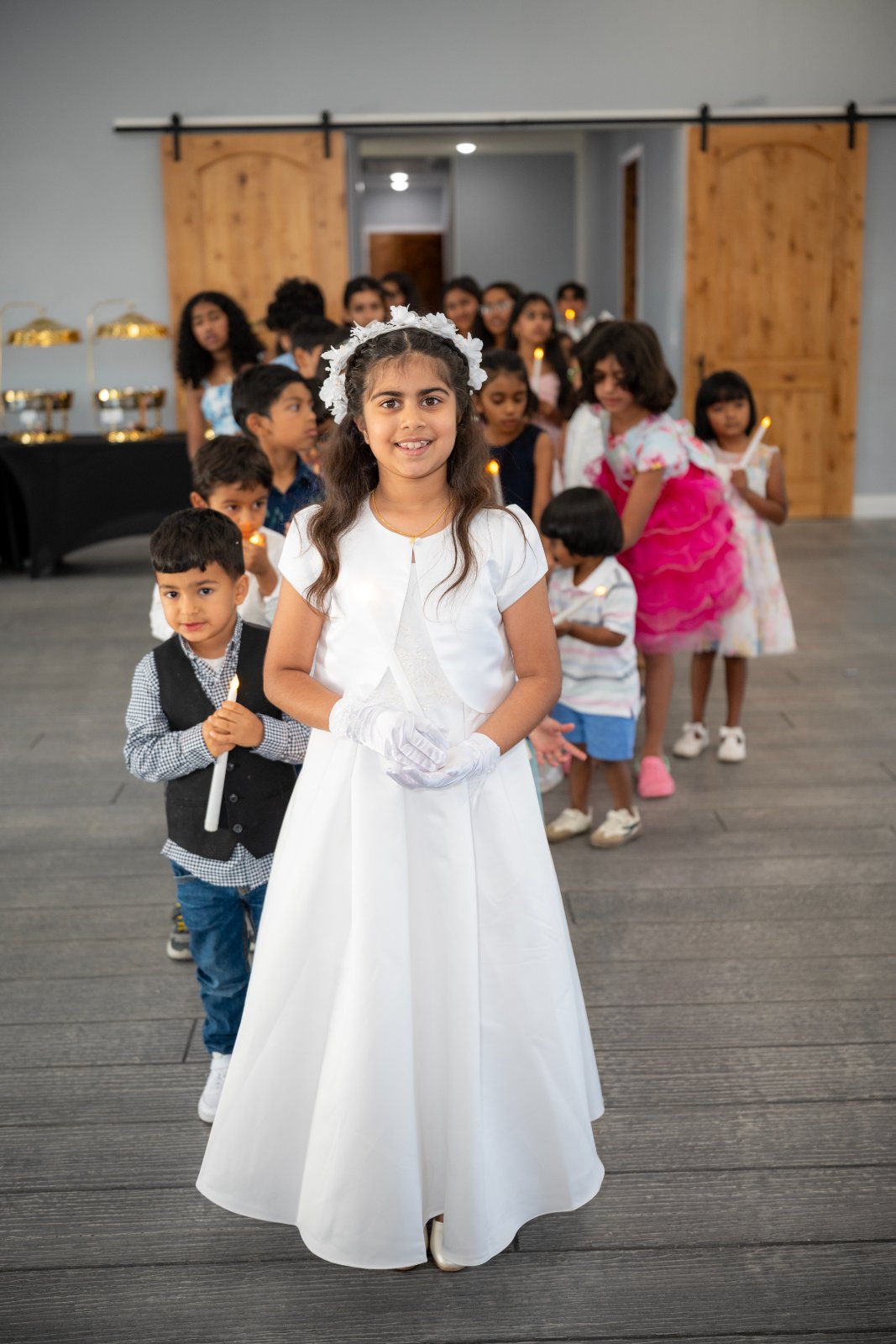 Children lined up holding candles during a First Communion celebration, with the lead girl in a white dress and floral headpiece, captured by Zan Visuals as part of event photography coverage.