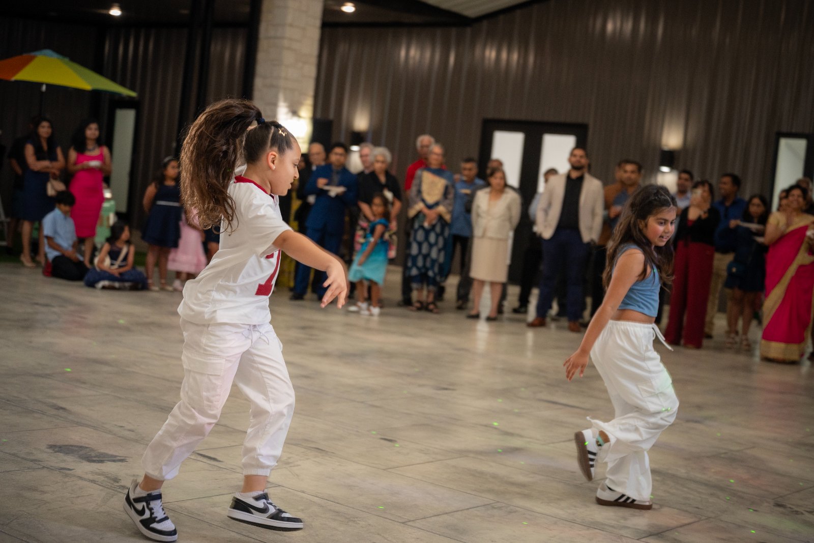 Two kids performing a dance routine during an indoor First Communion celebration, with guests watching in the background, captured by Zan Visuals as part of professional event photography.