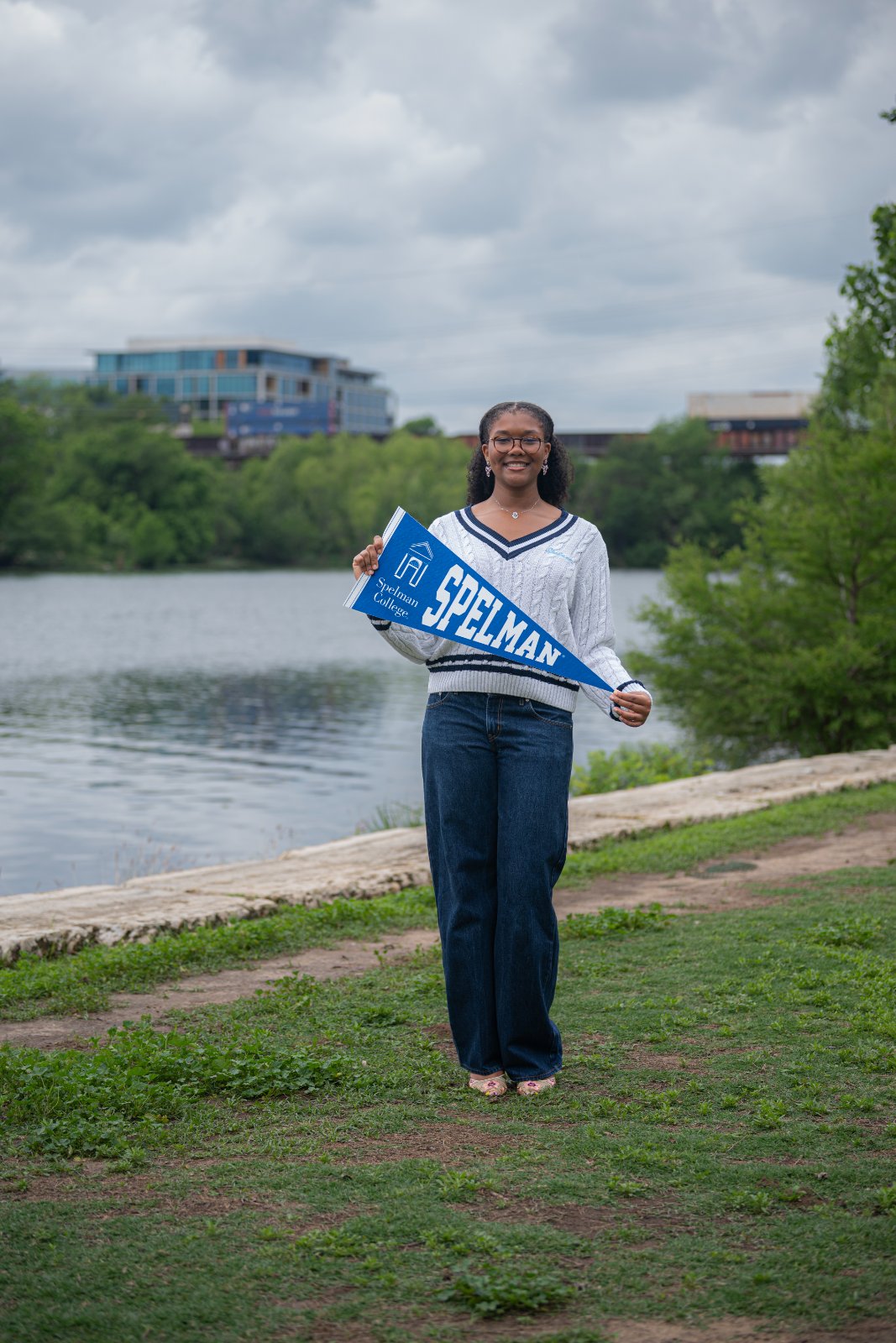 Graduate holding a Spelman College pennant during an outdoor photo session by the water, captured by Zan Visuals as part of a personalized graduation portrait session.