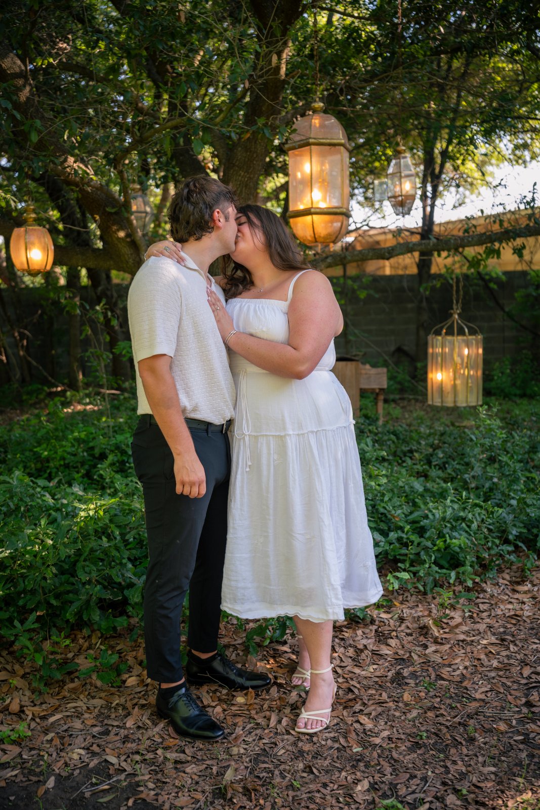 Romantic couple portrait kissing in a garden with warm lantern lights and greenery — taken by Zan Visuals.