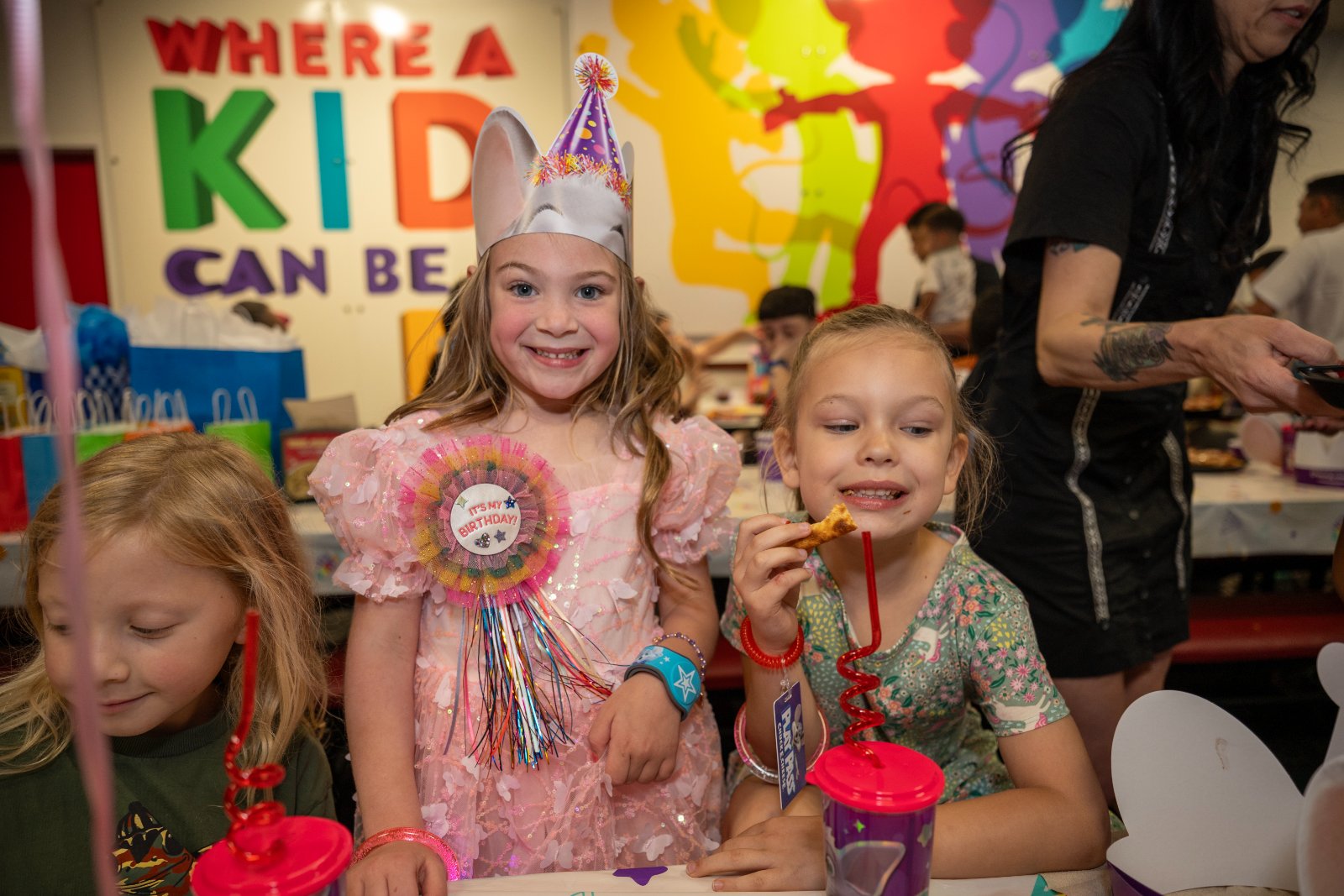 Birthday girl smiling and celebrating with friends at a colorful kids’ party, surrounded by food, drinks, and playful decorations — photographed by Zan Visuals.