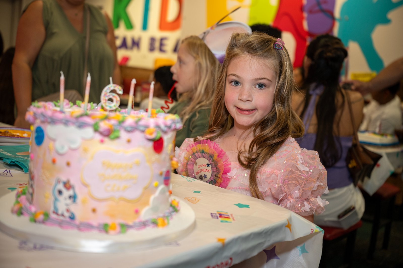 Birthday girl celebrating her sixth birthday with a decorated unicorn-themed cake, surrounded by friends in a colorful party setting — photographed by Zan Visuals.