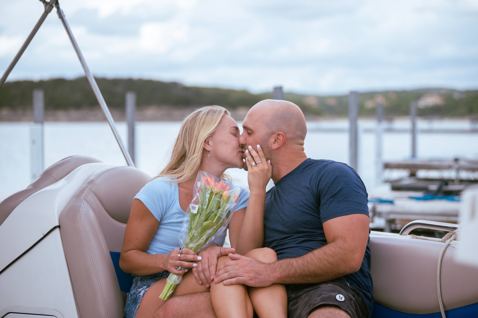 A couple sharing a romantic kiss on a lakeside boat while holding a bouquet during their engagement proposal session — captured by Zan Visuals.