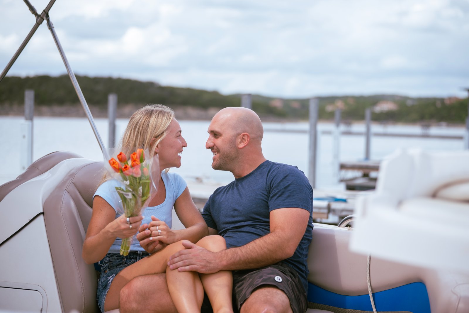 A couple sharing a warm moment on a boat as they hold hands and a bouquet of tulips during their lakeside proposal session — captured by Zan Visuals.
