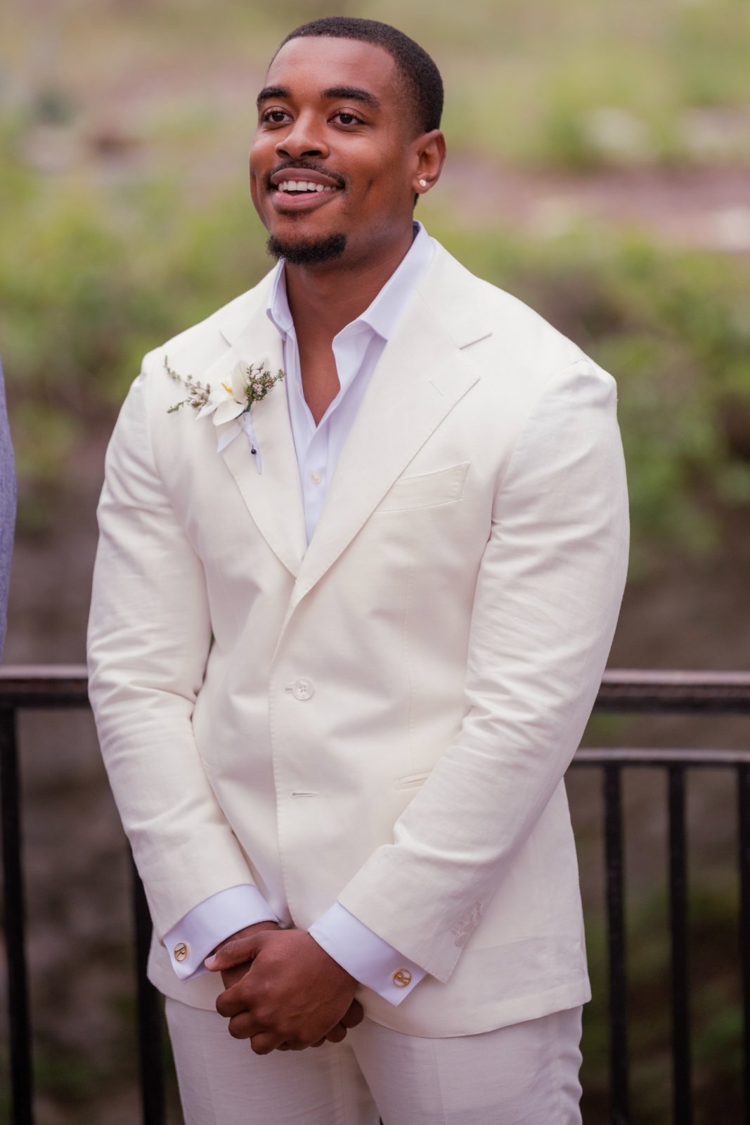 A groom wearing an off‑white suit standing outdoors with hands clasped, photographed in natural light by an Austin wedding photographer.