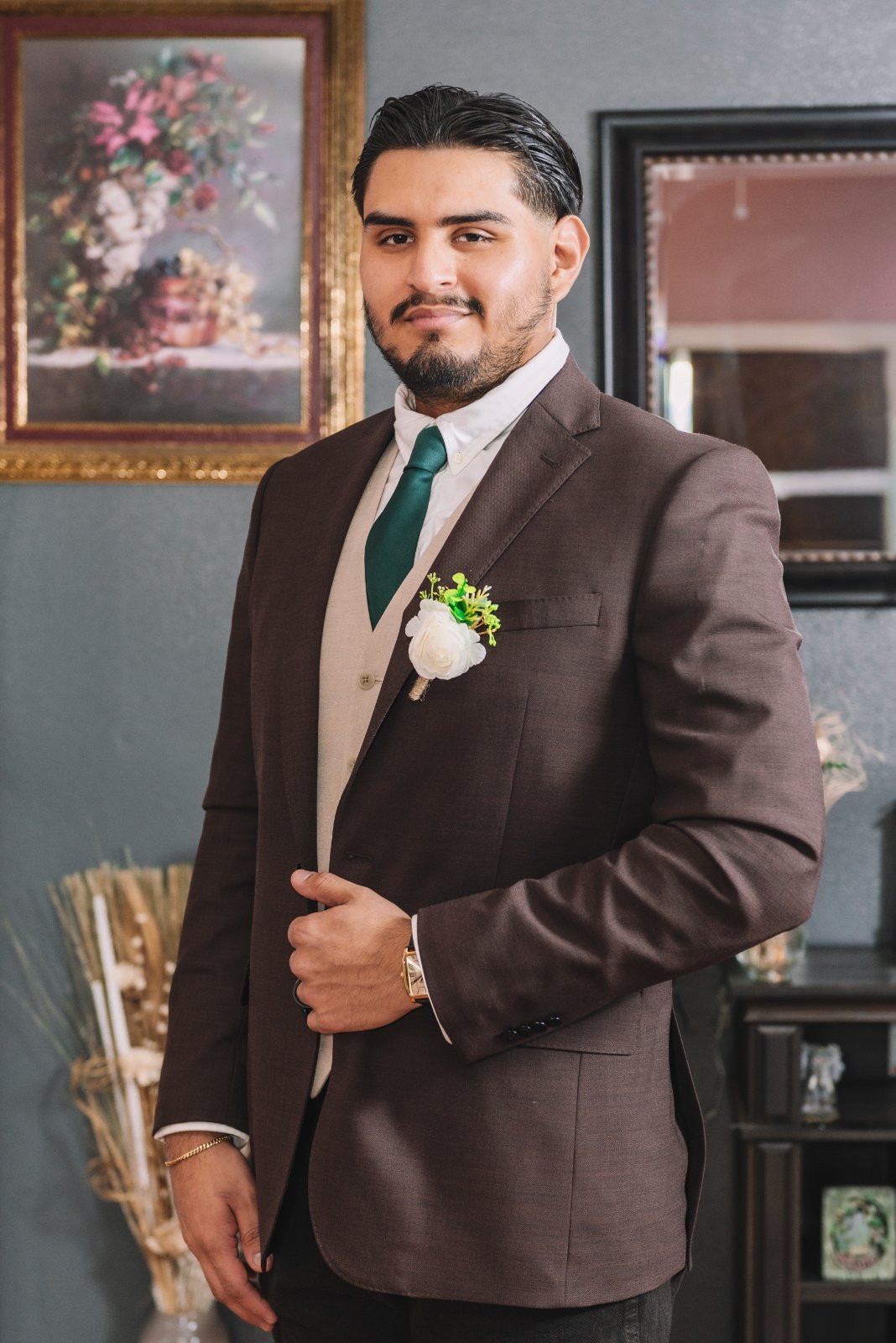 Groom standing indoors in a brown suit with a white boutonniere, posing for a classic wedding portrait captured by Zan Visuals.