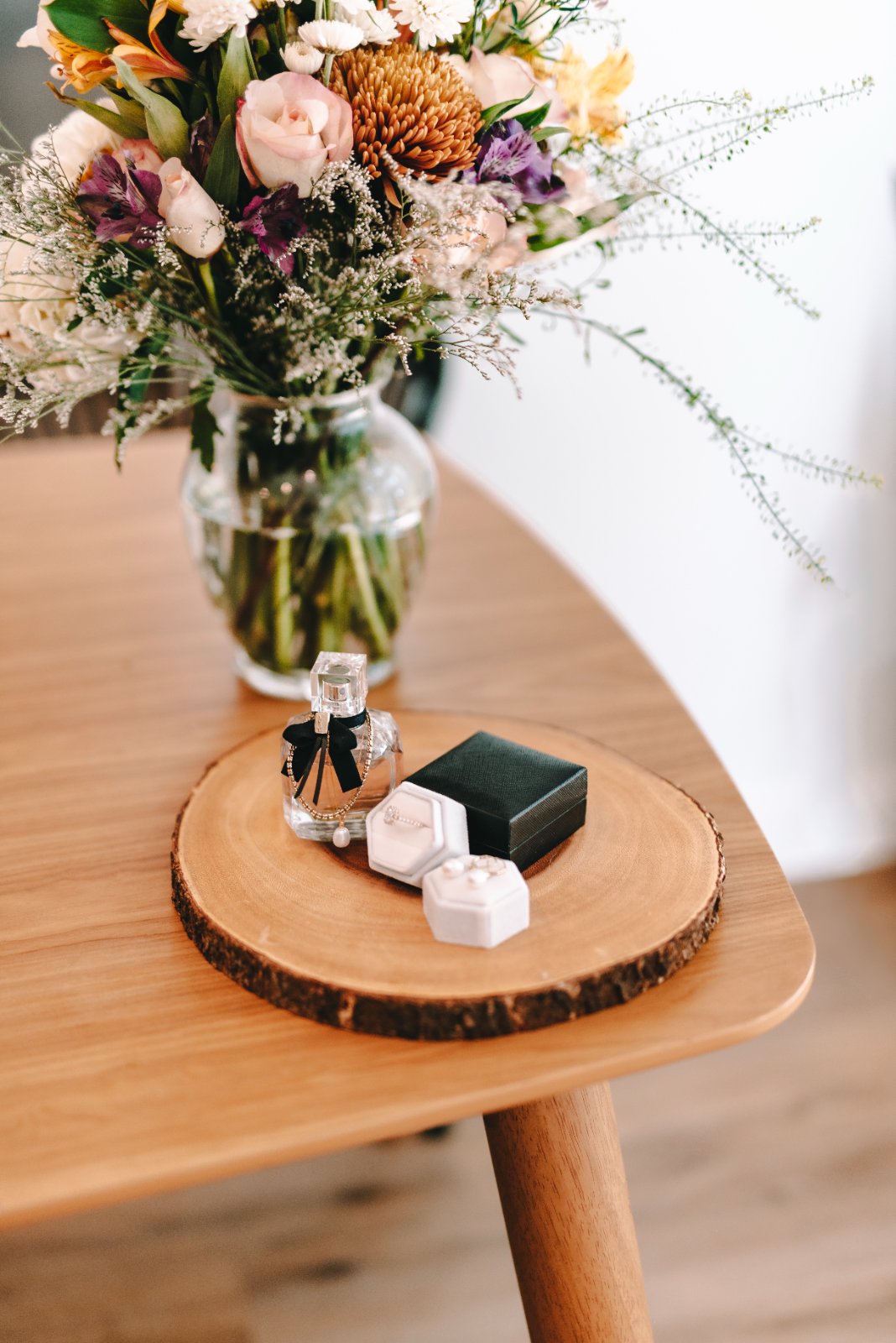 Wedding detail arrangement featuring a perfume bottle, ring boxes, and a floral bouquet on a wooden tray, captured by Zan Visuals.