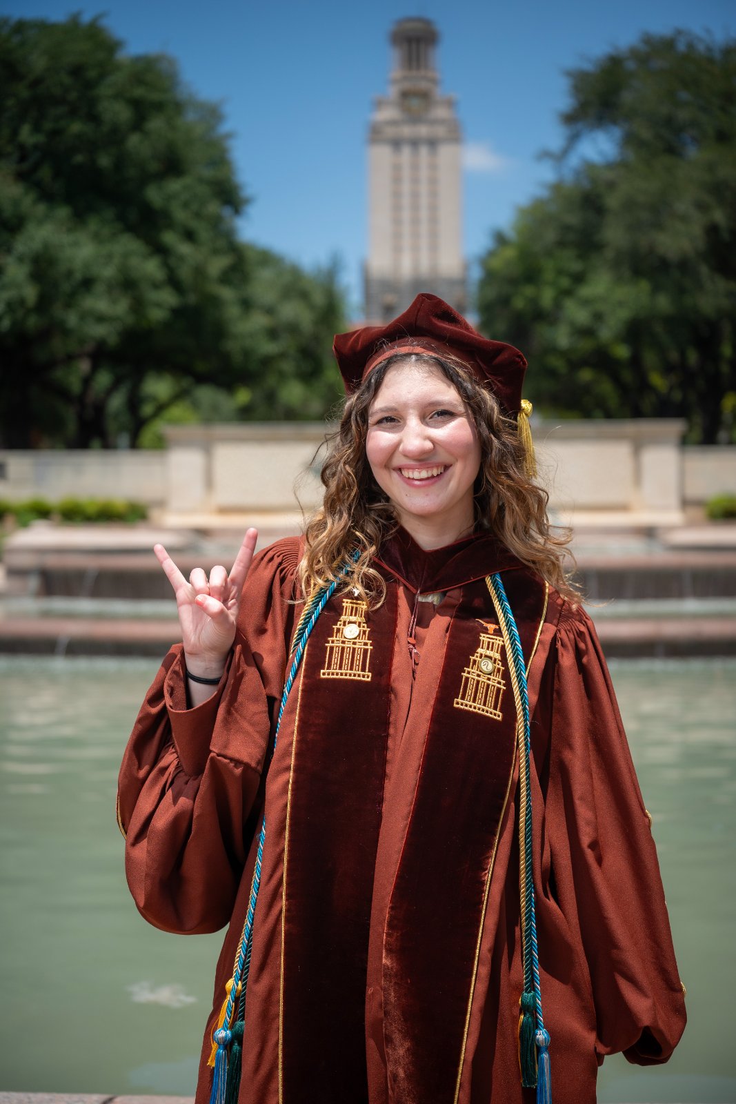 UT Austin graduation portrait with the Tower in the background and the graduate making the Hook ’Em Horns gesture — photographed by Zan Visuals.