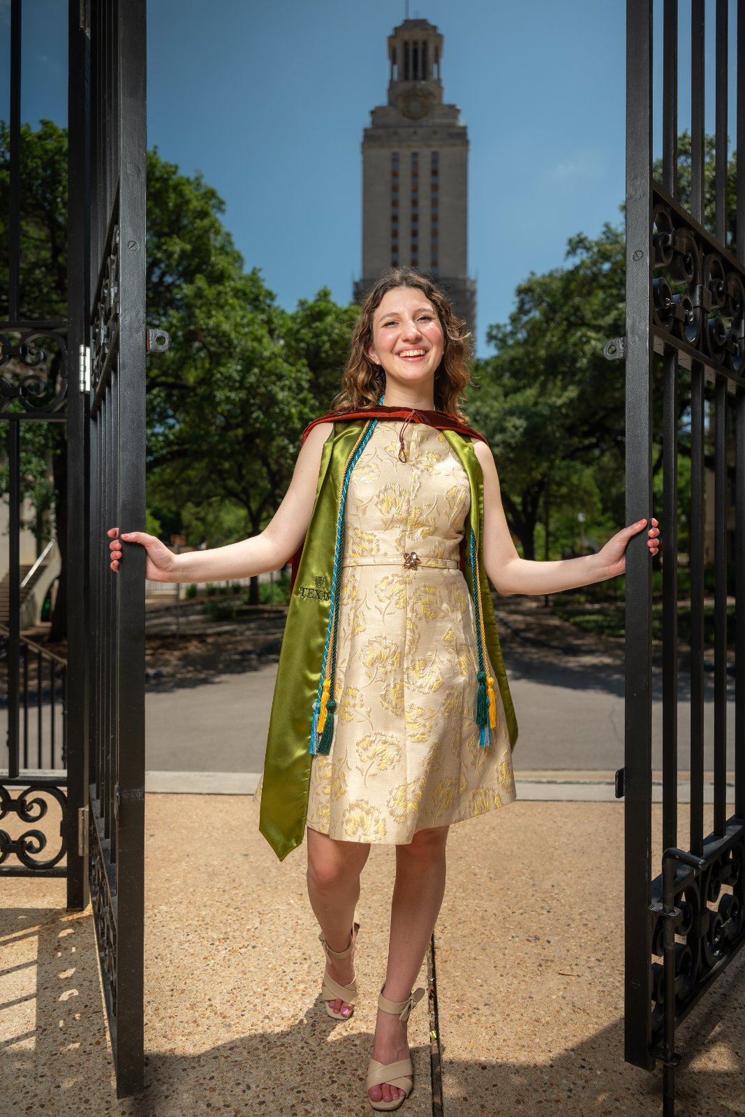 UT Austin graduation portrait of the graduate stepping through iron gates with the Tower in the background — photographed by Zan Visuals.
