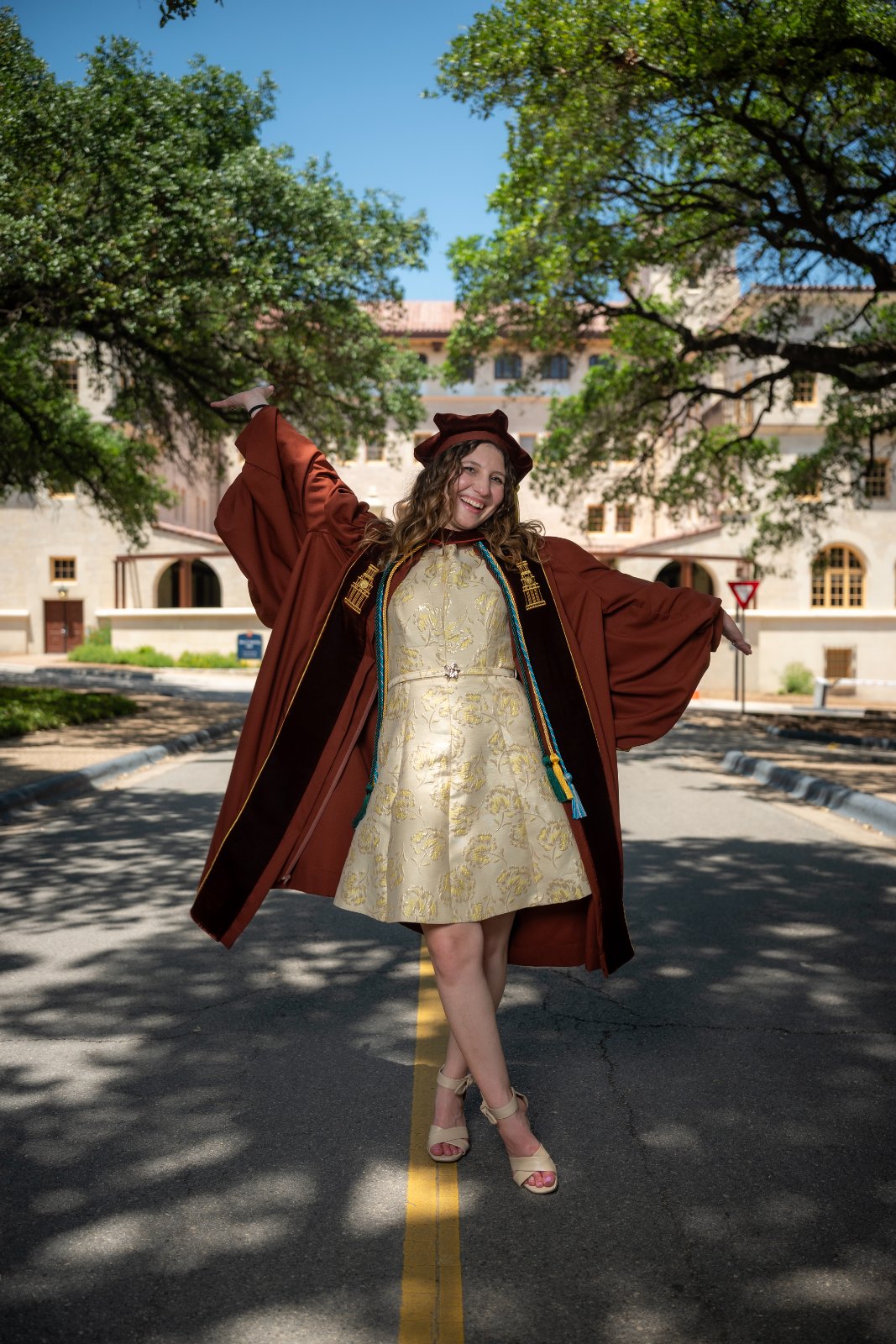 UT Austin graduation portrait of the graduate celebrating on a tree‑lined campus street with arms raised in joy — photographed by Zan Visuals.