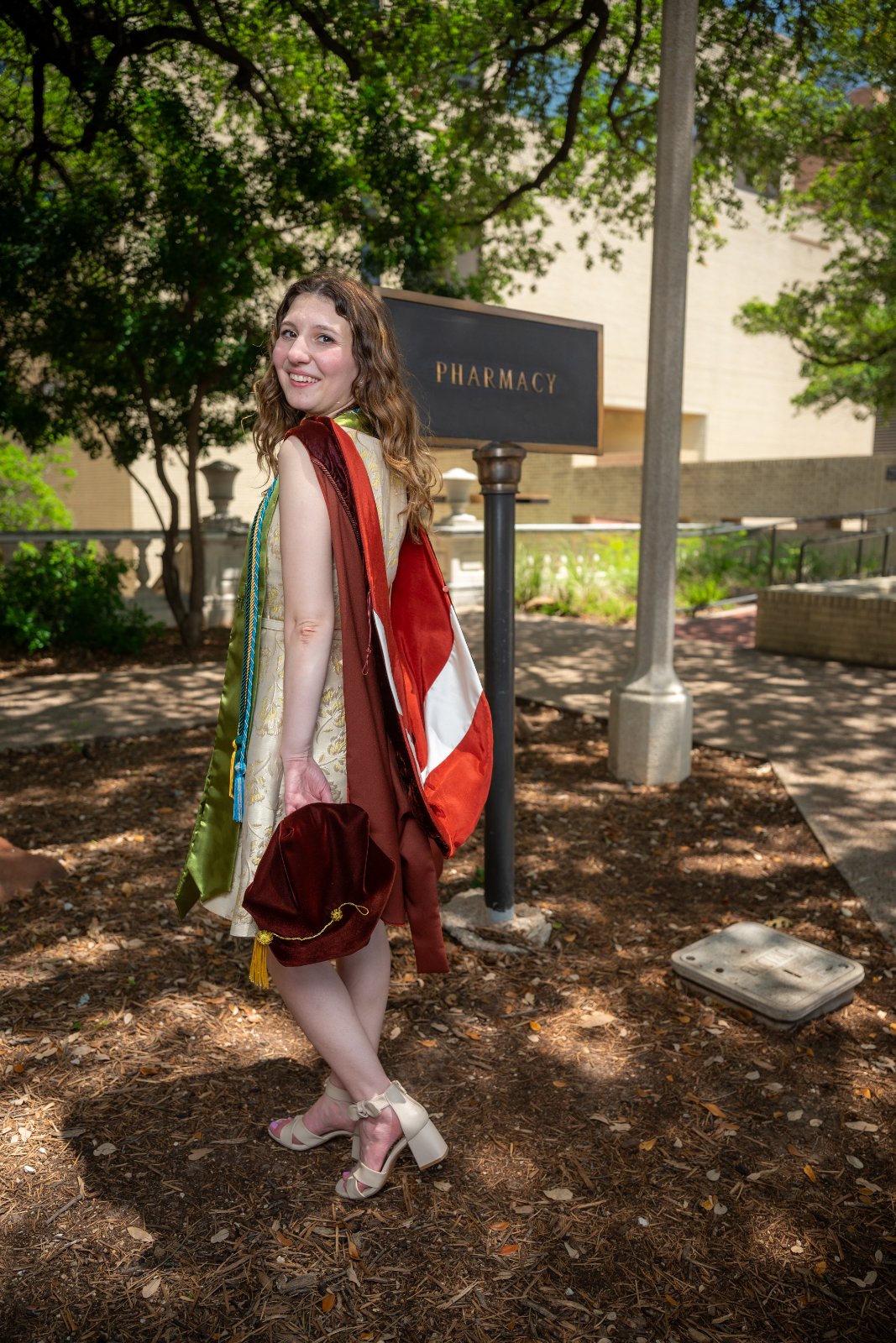 UT Austin pharmacy graduation portrait featuring the graduate in full regalia standing beside the Pharmacy sign — photographed by Zan Visuals.