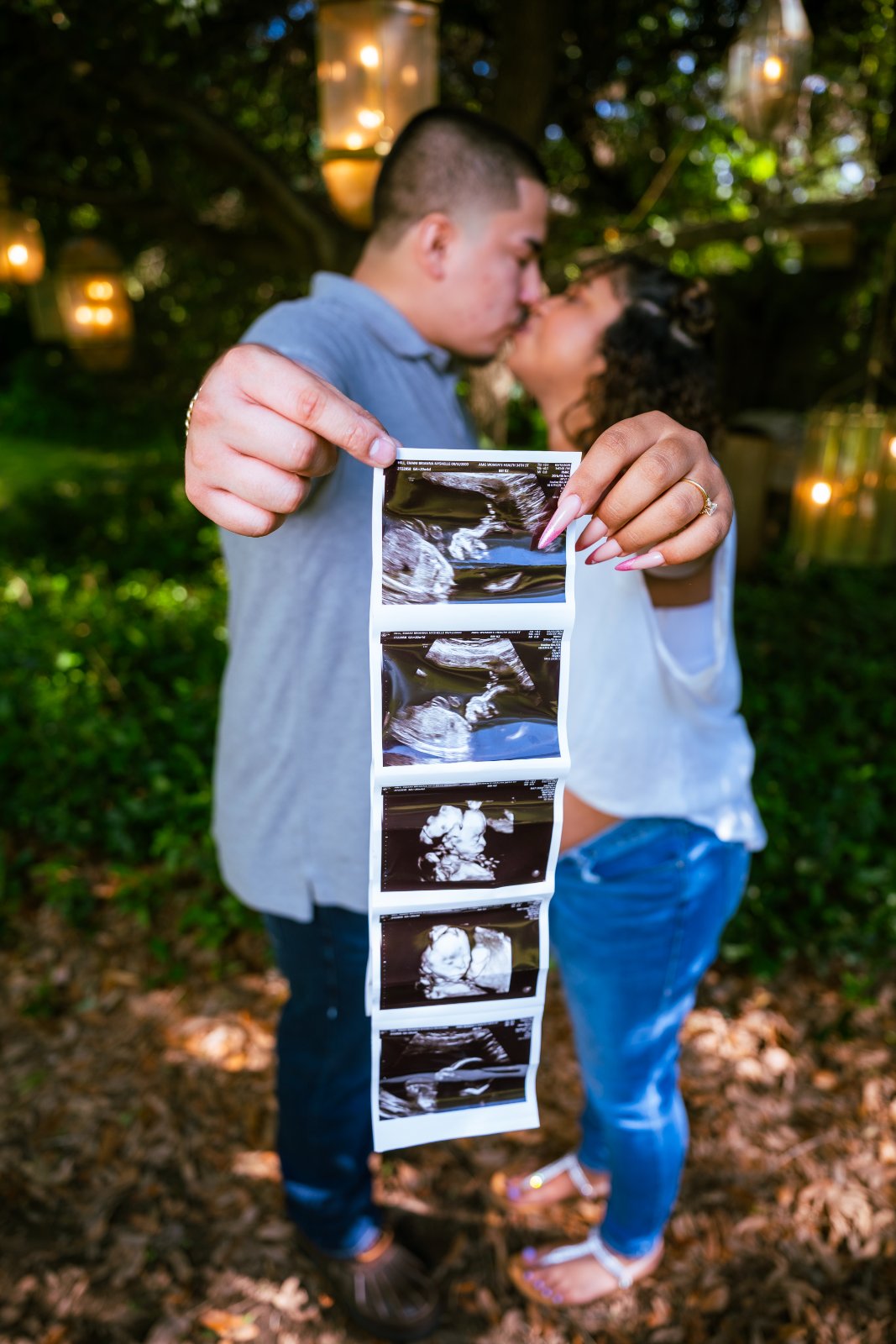 Couple holding ultrasound photos while sharing a kiss during a maternity photoshoot in a natural outdoor setting — photographed by Zan Visuals.