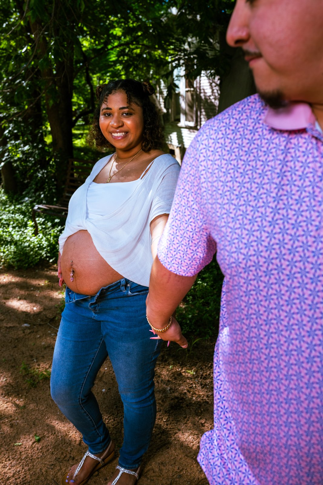 Couple holding hands with focus on the baby bump during a maternity photoshoot on a nature path surrounded by greenery — photographed by Zan Visuals.